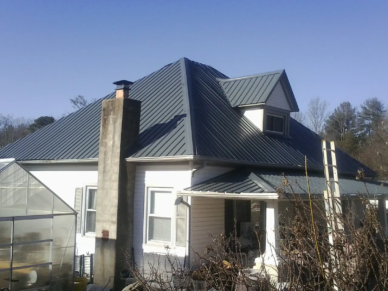 Dark blue standing seam metal roof on a white farmhouse with dormer — Slate & Tile Roof Repair by Roofing Brothers in Stanleytown