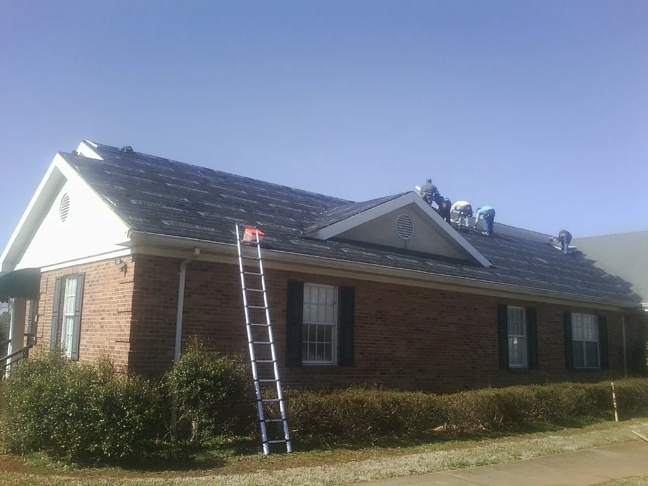 Crew tearing shingles off a brick ranch roof with a ladder set — Emergency Roof Repair work by our crew in Stanleytown