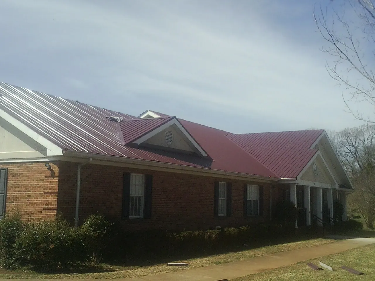 Red metal roof with gabled entries on a long brick building, from a Hail Damage Roof Repair job in Stanleytown
