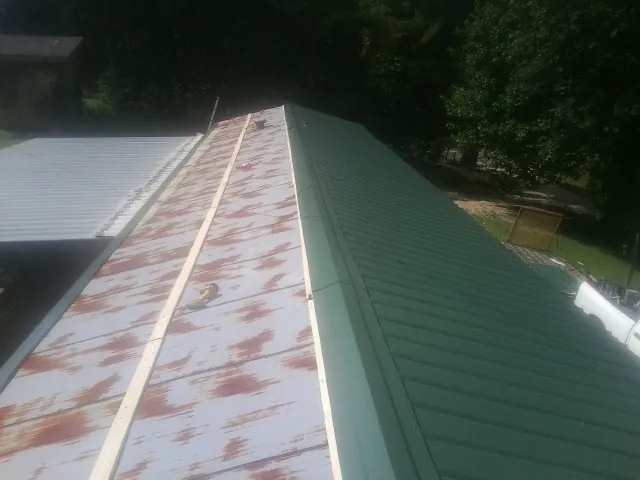 Old rusted panels beside newly installed green metal roofing — Wind Damage Roof Repair by Roofing Brothers in Stanleytown