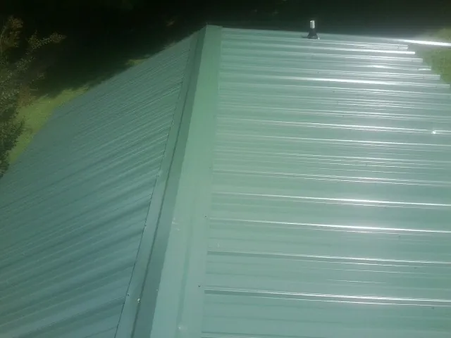 New green metal panels meeting at the ridge of a roof — Flat Roof Repair work by our crew in Stanleytown