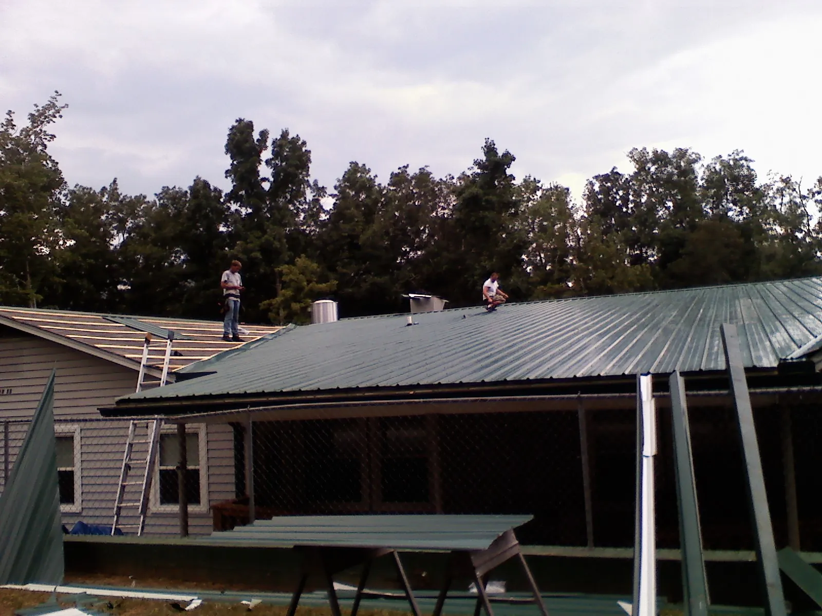 Two roofers installing green metal panels above a covered porch in Stanleytown