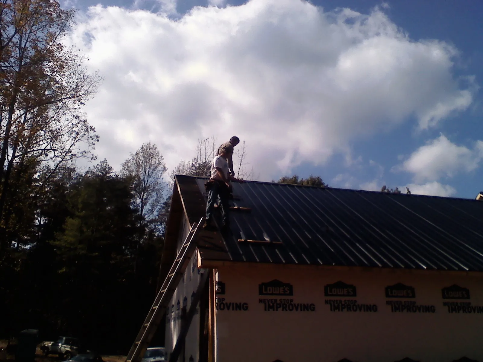 Roofer fastening dark metal panels high against a cloudy sky, from a Roof Inspection job in Stanleytown